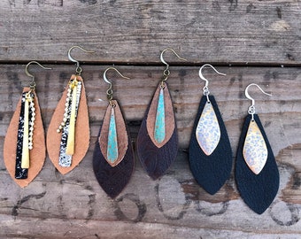 May include: Six pairs of leather earrings with different coloured leather and metal accents. The earrings are all teardrop shaped and have a silver or gold hook.