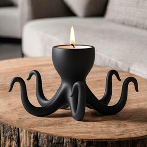May include: A black octopus-shaped candle holder with a lit candle. The candle holder is made of a matte black material and has eight curved tentacles. It sits on a wooden table, creating a unique decorative piece.