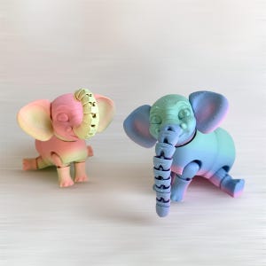 May include: Two small, colourful, 3D printed elephant toys with articulated limbs and a segmented trunk. The elephant on the left is pink and yellow, while the elephant on the right is blue and green.