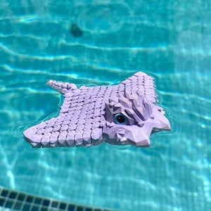 May include: A purple 3D printed stingray toy floating in a swimming pool. The stingray has a detailed, textured surface and a large, expressive eye.