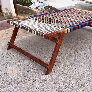 May include: A wooden bed frame with a woven top. The frame is a dark brown colour, and the woven top is a mix of colours including blue, red, and white. The bed is approximately 152 cm long.