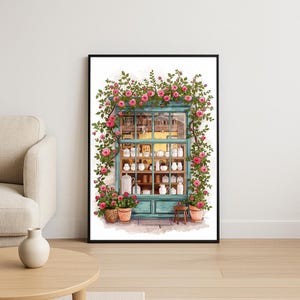 Könnte beinhalten: Aquarelldruck eines Schaufensters mit weißen Keramikartikeln. Das türkisfarbene Fenster ist von rosa Rosen und grünen Ranken umrahmt. Blumentöpfe und ein kleiner Holzschemel befinden sich am unteren Rand des Fensters.