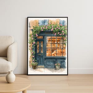 Puede incluir: Pintura a la acuarela de una panadería con puerta y marcos de ventanas azules. La tienda está adornada con rosas rosas y enredaderas verdes. La ventana muestra productos de panadería. La palabra "Tante B" está escrita encima de la ventana.