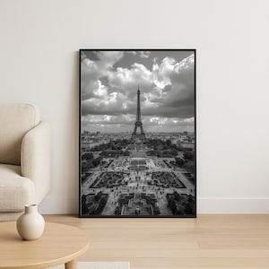Peut inclure: Tirage encadré en noir et blanc de la Tour Eiffel à Paris. La photo capture le monument emblématique d'en haut, révélant les jardins et le paysage urbain sous un ciel nuageux. L'impression est présentée dans un cadre noir.