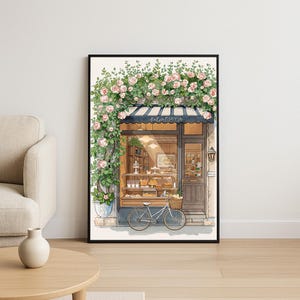 Könnte beinhalten: Aquarelldruck einer charmanten Patisserie mit schwarzer Markise und Fahrrad davor. Das Geschäft ist mit Kletterrosen geschmückt und zeigt Gebäck. Das Wort "Patisserie" steht über dem Eingang.