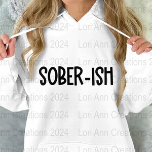 Puede incluir: Sudadera con capucha blanca con el texto "SOBER-ISH" impreso en negro en la parte delantera.