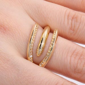 May include: A gold-toned ring featuring three distinct bands. The outer bands are textured with small, bead-like details, while the central band is smooth and polished. The design incorporates a light, neutral-colored inlay between the metal bands.