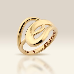 May include: A polished gold ring featuring an open, fluid design with two interlocking, smooth, curved bands that create a continuous, rounded shape. The metal has a high-shine finish, reflecting light across its surface, with a hollow center.