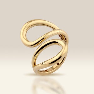 Könnte beinhalten: Ein goldfarbener Ring mit einem einzigartigen, fließenden Design. Der Ring hat zwei ineinander verschlungene Schlaufen, die eine offene, abstrakte Form bilden. Die polierte Oberfläche reflektiert das Licht und unterstreicht die glatten Kurven und die allgemeine Eleganz. Der Ring ist ein Schmuckstück.