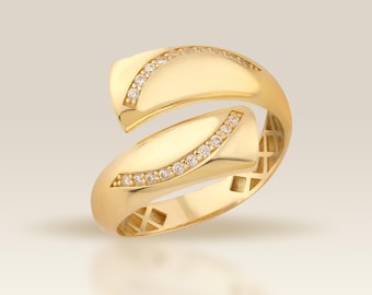 May include: A gold-colored ring with a unique, open design. The ring features two curved bands that overlap, each adorned with a row of small, sparkling gemstones. The ring's surface reflects light, highlighting its polished finish.