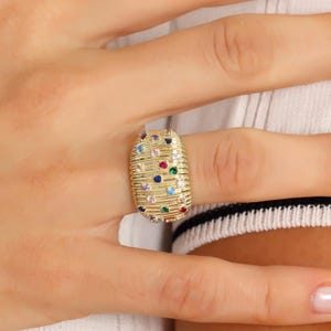 Detailed jewelry shot of a bold gold dome ring resting on a neutral white display surface to accent its textured surface geometry.