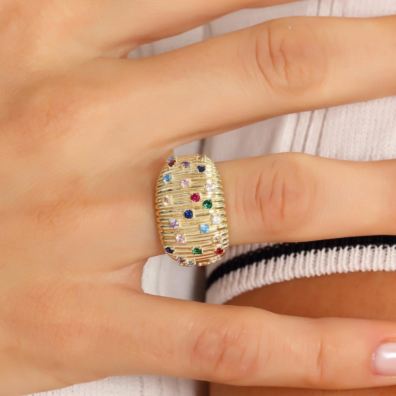 Detailed jewelry shot of a bold gold dome ring resting on a neutral white display surface to accent its textured surface geometry.