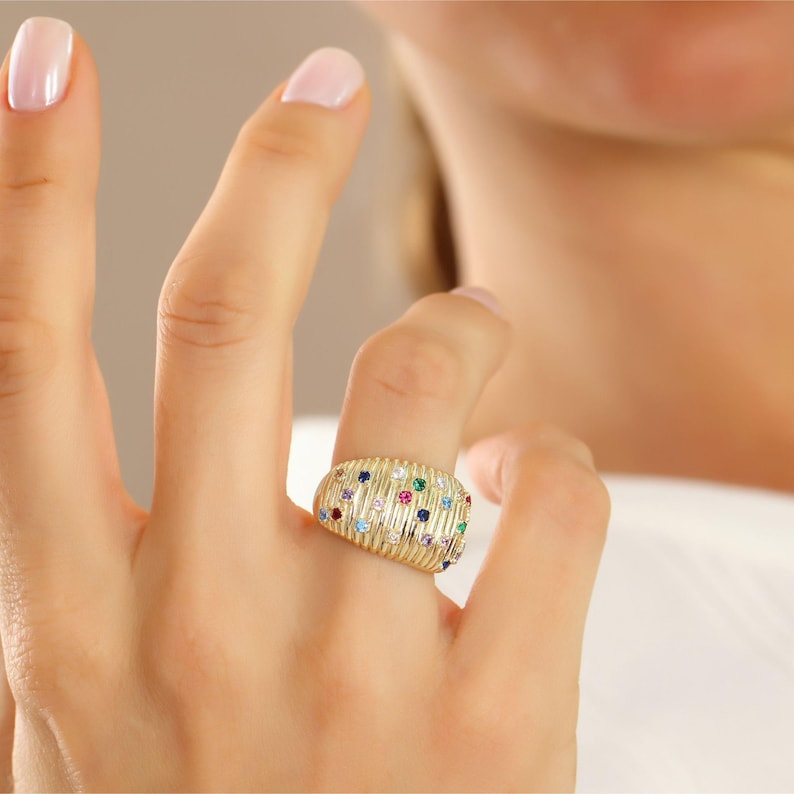 Front-facing studio capture of a polished 14K gold fluted ring emphasizing the rhythmic alignment of ruby, emerald, sapphire, and amethyst stones.