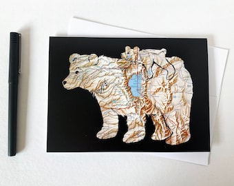 May include: A black card with a brown bear and a smaller brown bear cub on top of it. The bears are made of a map with brown, white, and blue colors. The background is black.
