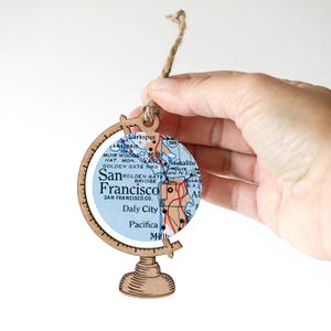 May include: Wooden globe ornament with a map of San Francisco, California. The globe is brown and has a string for hanging. The map shows the Golden Gate Bridge, Sausalito, and other landmarks.