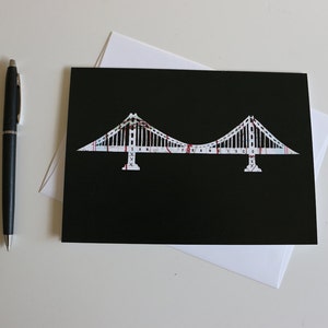 May include: A black card with a white silhouette of the Golden Gate Bridge, with the words "SAN FRANCISCO" printed on the bridge.