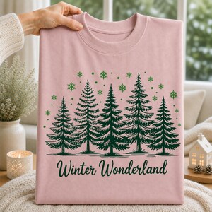 Winter Wonderland pine forest and snowflake shirt design displayed on a soft pink T-shirt for a feminine winter apparel style