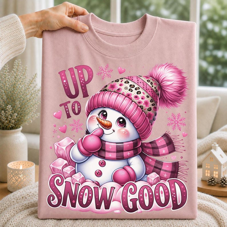 Pink t-shirt featuring a playful snowman in a pink winter hat and scarf with Up to Snow Good lettering and pink snowflakes