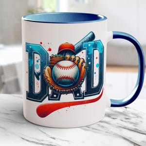 May include: White ceramic mug with a blue interior and handle, featuring the word "DAD" in blue with baseball-themed graphics. The design includes a baseball, glove, helmet, and bat, with red accents.