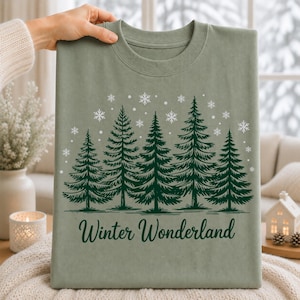 Winter Wonderland pine tree and snowflake graphic printed on a sage green T-shirt for a cozy winter apparel look