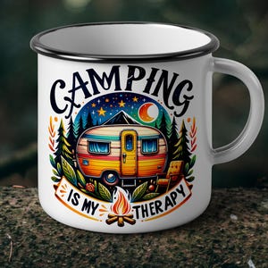 May include: White enamel camping mug with a black rim and handle. The mug features a colourful illustration of a camper, trees, and a campfire, with the text "CAMPING IS MY THERAPY".