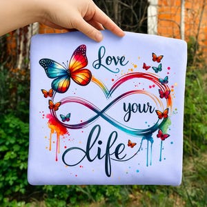 May include: A light blue square with a colorful butterfly and the words "Love your life" in a cursive font. The design includes an infinity symbol and several small butterflies in various colors.