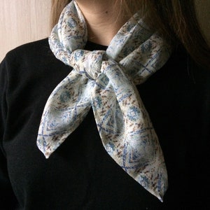 May include: A white scarf with a blue and brown geometric pattern tied around the neck in a knot.