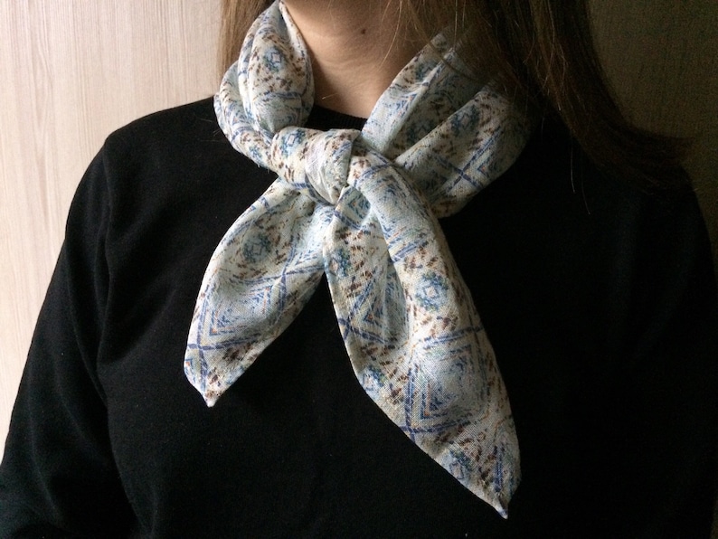 May include: A white scarf with a blue and brown geometric pattern tied around the neck in a knot.