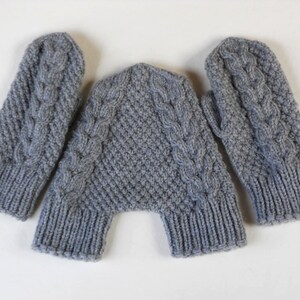K&ouml;nnte beinhalten: Ein Paar graue Strickhandschuhe mit einem Zopfmuster. Die Handschuhe liegen flach auf einer wei&szlig;en Oberfl&auml;che.