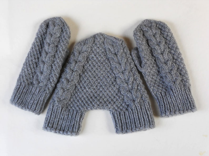 K&ouml;nnte beinhalten: Ein Paar graue Strickhandschuhe mit einem Zopfmuster. Die Handschuhe liegen flach auf einer wei&szlig;en Oberfl&auml;che.