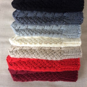 K&ouml;nnte beinhalten: Ein Stapel von acht gestrickten Handw&auml;rmern in verschiedenen Farben, darunter Schwarz, Grau, Wei&szlig;, Beige, Rot und Burgunderrot. Die Handw&auml;rmer sind mit einem Zopfmuster gestrickt.