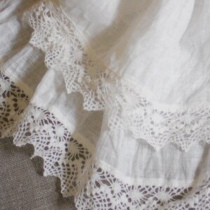 May include: White fabric with two layers of delicate white lace trim. The lace has a scalloped edge and a floral pattern.
