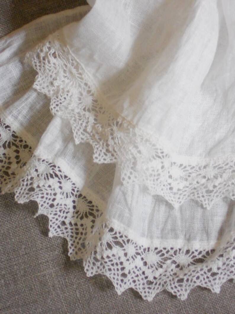 May include: White fabric with two layers of delicate white lace trim. The lace has a scalloped edge and a floral pattern.