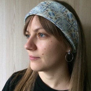 May include: A woman with long brown hair is wearing a blue and brown patterned headband. She is wearing a black shirt and has a silver hoop earring in her left ear.