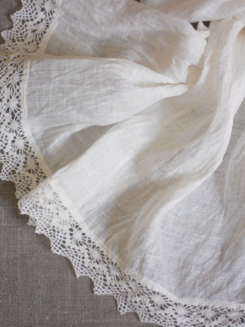 May include: White linen fabric with a delicate lace trim. The fabric is soft and flowing, with a slightly textured surface.