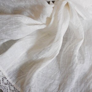 May include: White linen fabric with a delicate lace trim. The fabric is soft and flowing, with a subtle texture.