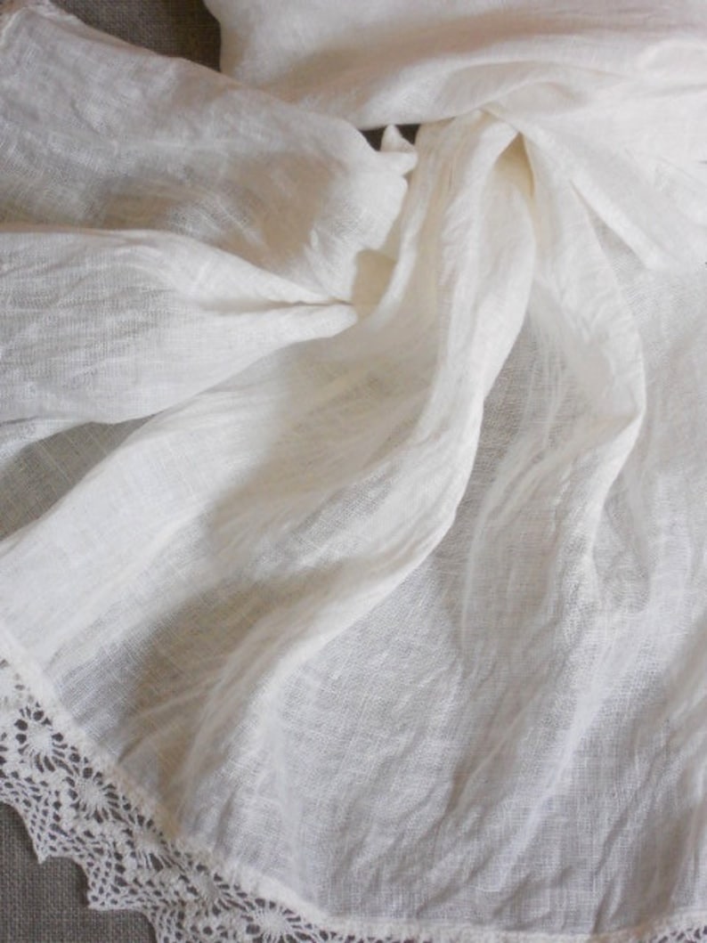 May include: White linen fabric with a delicate lace trim. The fabric is soft and flowing, with a subtle texture.