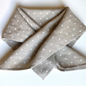 May include: A beige linen tea towel with white polka dots folded into a triangle shape.