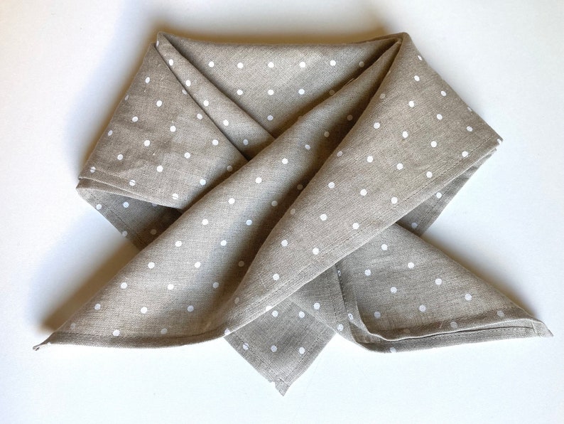 May include: A beige linen tea towel with white polka dots folded into a triangle shape.