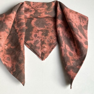 Peut inclure: Une écharpe triangulaire avec un motif tie-dye dans les tons de brun et de rose.