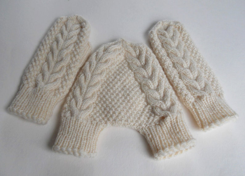 K&ouml;nnte beinhalten: Ein Paar wei&szlig;e Strickhandschuhe mit einem Zopfmuster. Die Handschuhe sind durch eine Strickband verbunden.