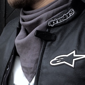May include: A black leather motorcycle jacket with white stitching and a gray scarf. The jacket has a large white star logo with the text "alpinestars" on the collar.