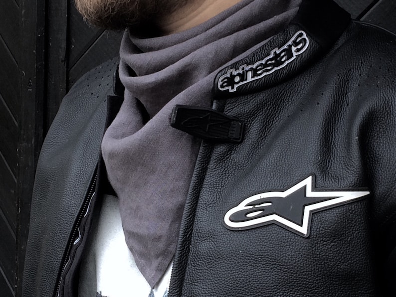 May include: A black leather motorcycle jacket with white stitching and a gray scarf. The jacket has a large white star logo with the text "alpinestars" on the collar.
