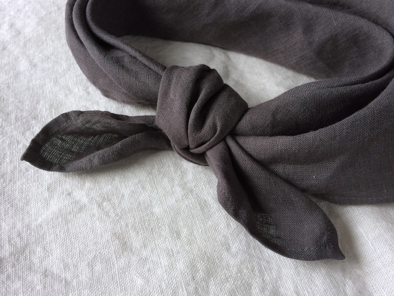 May include: A dark gray linen bandana tied in a knot. The bandana is made of a soft, textured fabric.