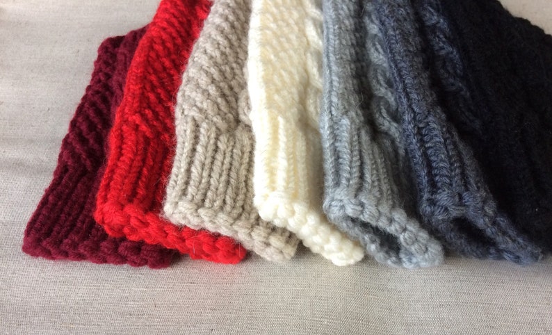K&ouml;nnte beinhalten: Ein Stapel von sechs gestrickten M&uuml;tzen in verschiedenen Farben, darunter Burgunderrot, Rot, Beige, Wei&szlig;, Grau und Dunkelgrau. Die M&uuml;tzen sind alle mit einem Zopfmuster gestrickt.