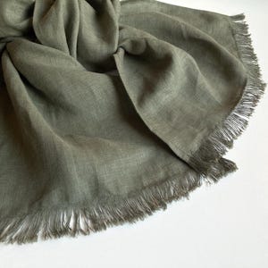 Może przedstawiać: Miękki, zielony szal z frędzlami. Szal wykonany jest z lekkiej tkaniny i idealnie nadaje się do dodania odrobiny koloru do każdego stroju.