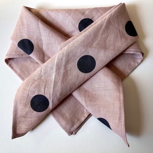 May include: A pink linen bandana with black polka dots. The bandana is folded into a triangular shape.
