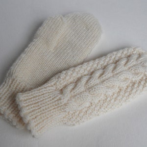 K&ouml;nnte beinhalten: Ein Paar wei&szlig;e Strickhandschuhe, einer mit einem Zopfmuster und der andere mit einem glatten Strickmuster.