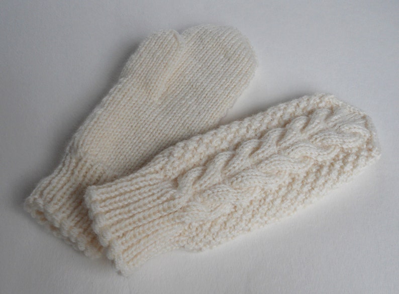 K&ouml;nnte beinhalten: Ein Paar wei&szlig;e Strickhandschuhe, einer mit einem Zopfmuster und der andere mit einem glatten Strickmuster.