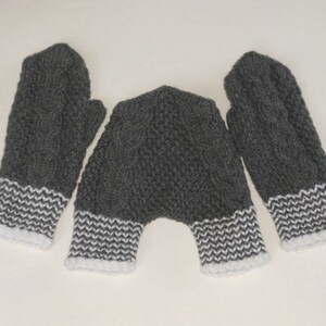 K&ouml;nnte beinhalten: Ein Paar graue Strickhandschuhe mit wei&szlig;em Besatz. Die Handschuhe haben ein Zopfmuster.